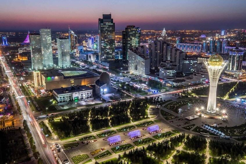 A cityscape at night with illuminated buildings, a prominent tower, and a well-lit roundabout with decorative lighting. 5