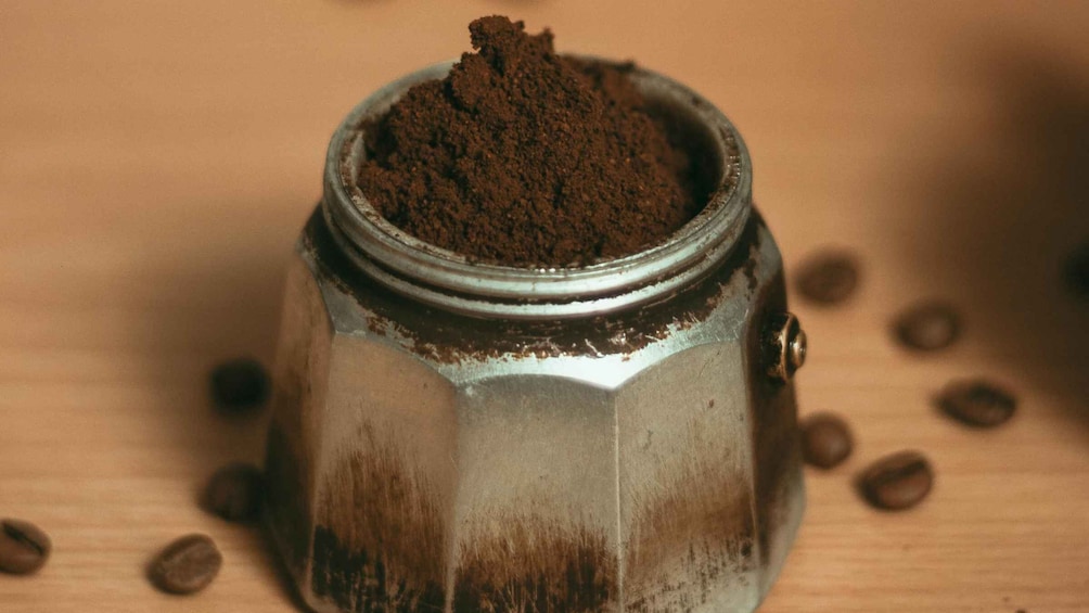 A metal container filled with brown powder, surrounded by coffee beans on a wooden surface. 2