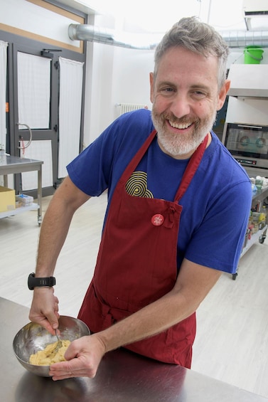 A man in a blue shirt and red apron mixing ingredients in a metal bowl. 4