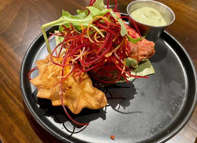 A plate with a fried item, possibly a fish, garnished with shredded vegetables and a leafy green, accompanied by a small bowl of sauce. 1