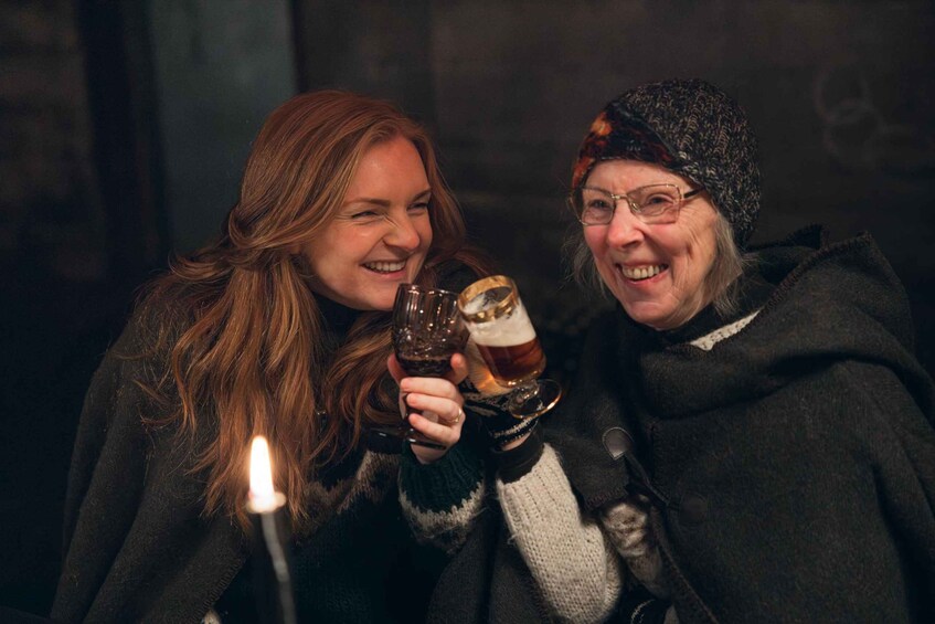 Two individuals holding glasses of beer, with a candle in the foreground. 1