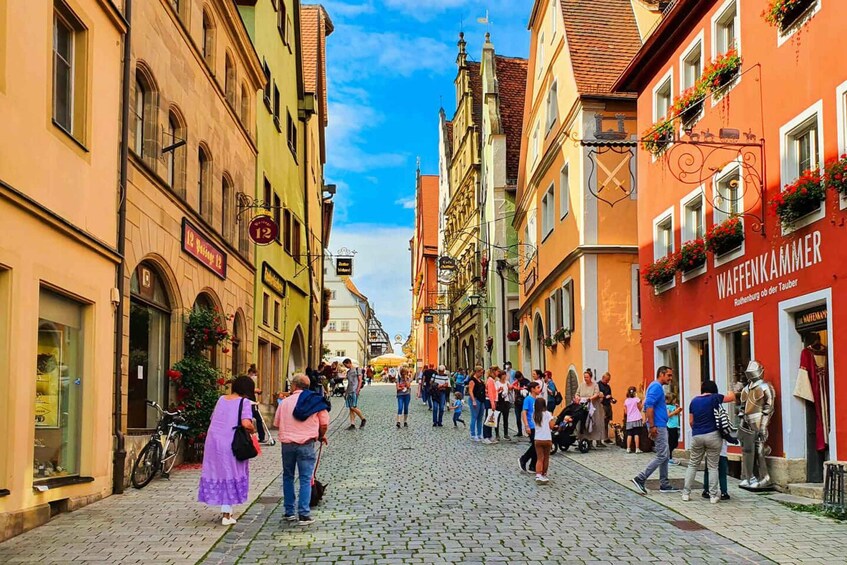 A cobblestone street lined with colorful buildings, a crowd of people, and a knight in armor. 3