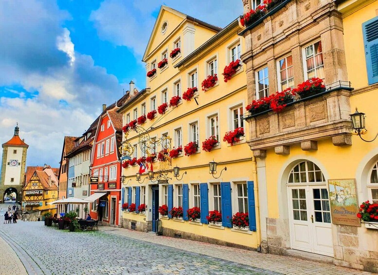 A cobblestone street lined with colorful buildings, some with flower boxes and a clock tower in the background. 5