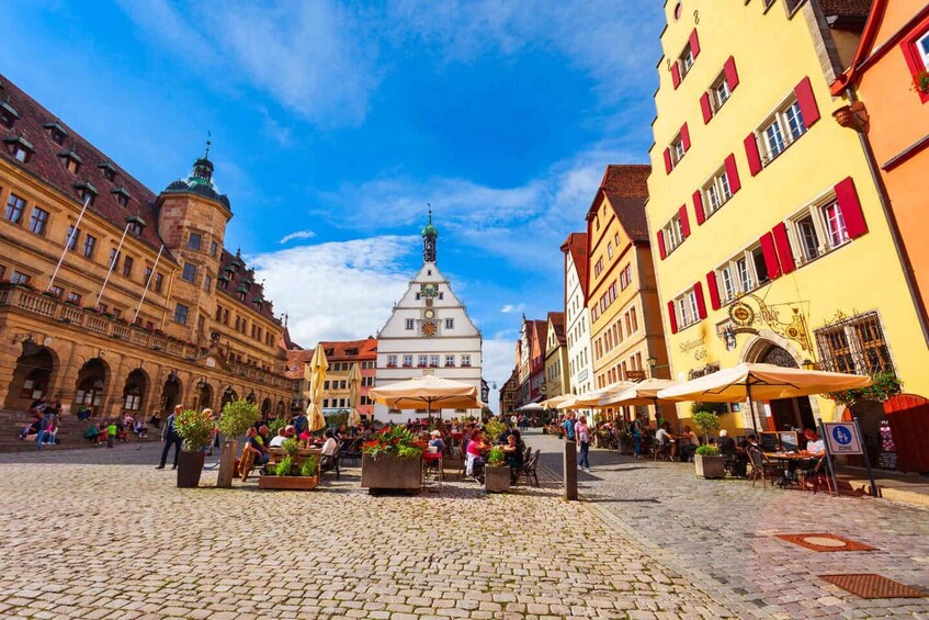 A cobblestone square with historic buildings, outdoor seating, and a prominent church tower. 4