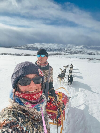A snowy landscape with a dog sled team and a person in a patterned coat. 2