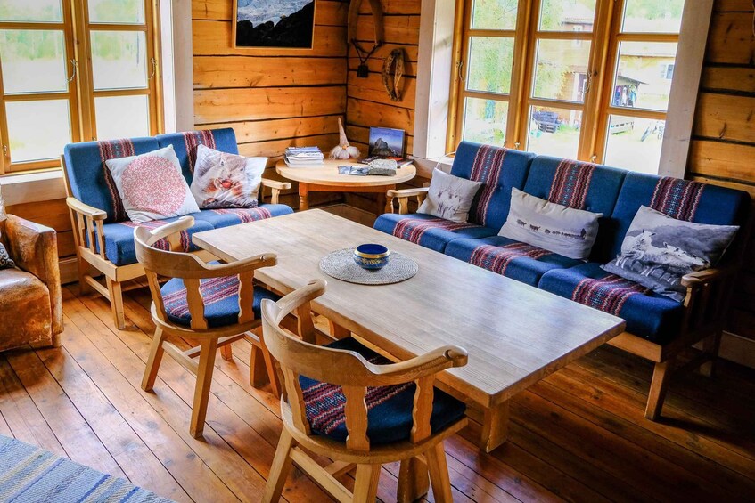 A cozy cabin interior with wooden walls, a blue sofa, a wooden table, and a wooden chair. 4