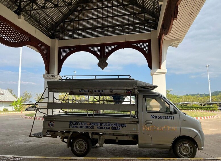 A tuk-tuk parked under a covered structure with a sign indicating 'Friend Ship Bridge' and 'HOUAYXAI URBAN'. 3
