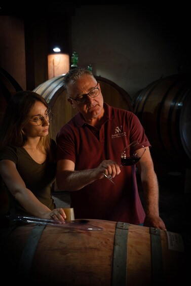 Two people standing by a wooden barrel, one holding a wine glass. 5