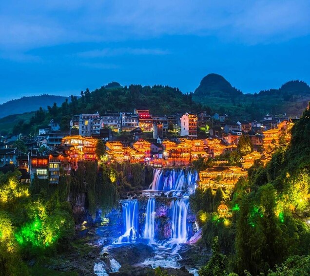 A town with traditional architecture, a waterfall, and a mountainous backdrop. 4