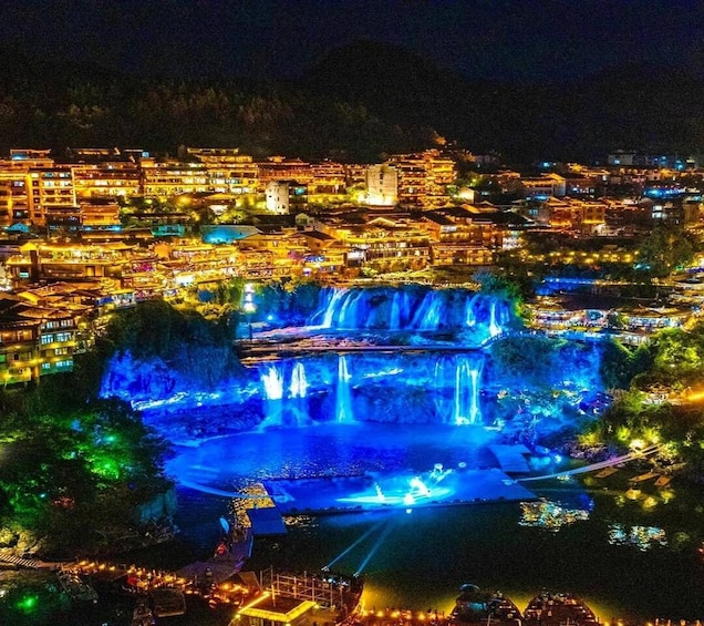 A night view of a town with illuminated buildings and a waterfall. 1