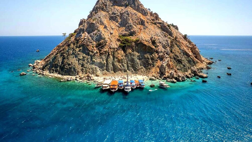 A rocky island with clear blue waters and boats docked at its base. 3
