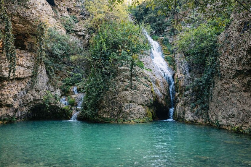 A waterfall cascading into a clear pool surrounded by rocky cliffs and lush greenery. 1