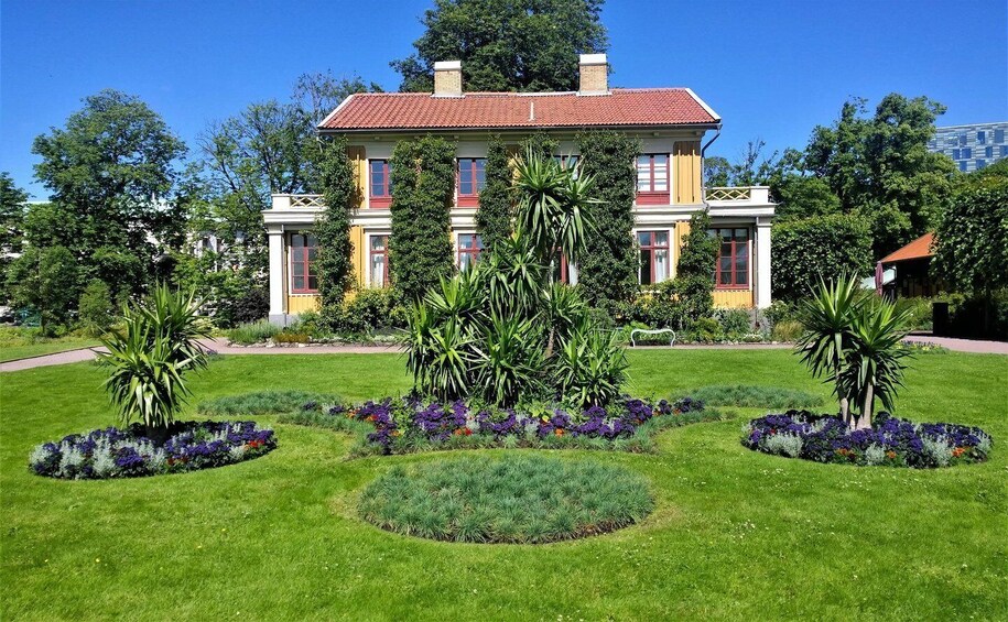A large, two-story building with a red-tiled roof, surrounded by well-maintained gardens and trees. 3