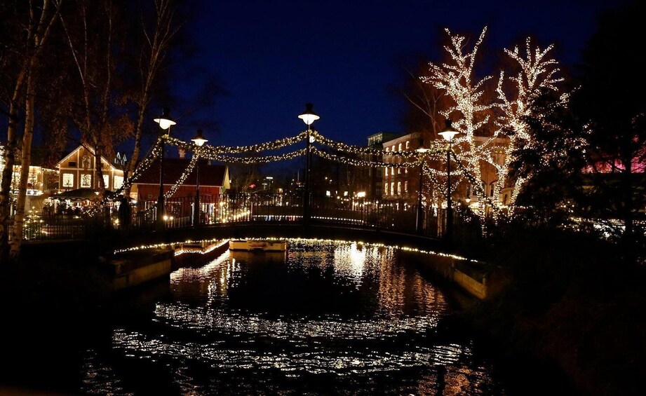 A nighttime scene with a bridge over water, decorated with lights and surrounded by buildings. 2