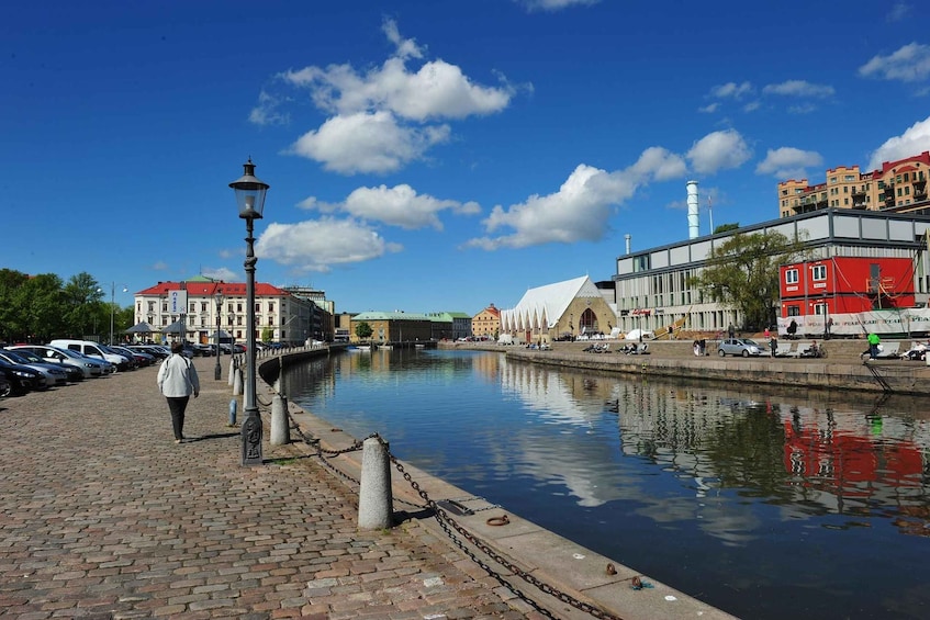 A riverside walkway with cobblestone pavement, a lamppost, and buildings with red roofs. 1