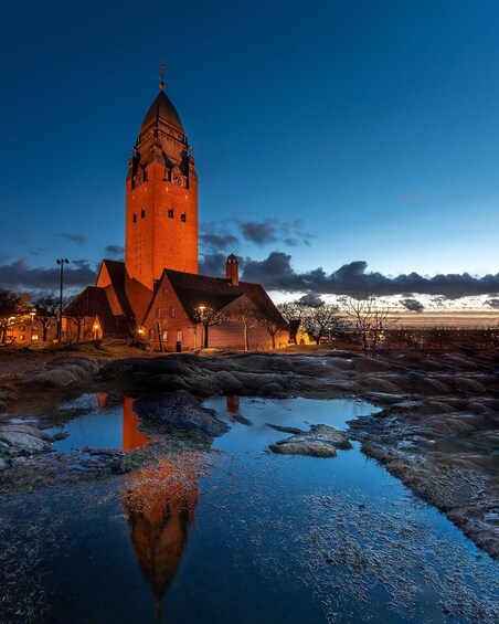 A historic tower with a clock, surrounded by traditional buildings and a reflective water body. 5