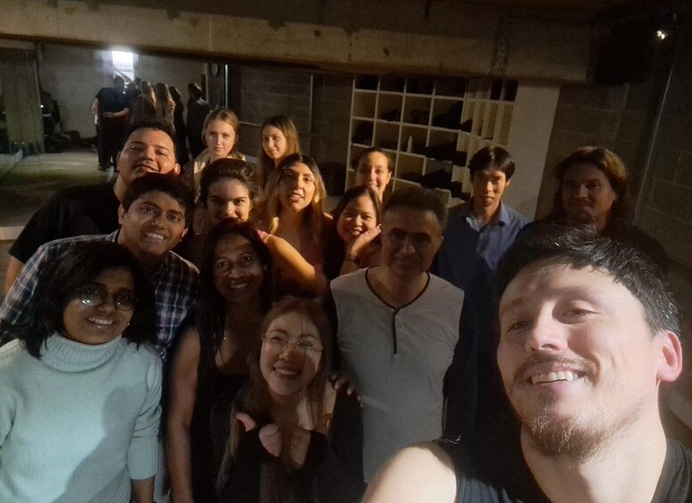 A group of people posing for a photo in an indoor setting with a concrete wall and a window in the background. 2