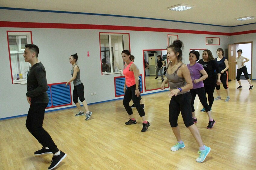 A group of people in a dance studio with wooden floors and mirrors on the walls. 3