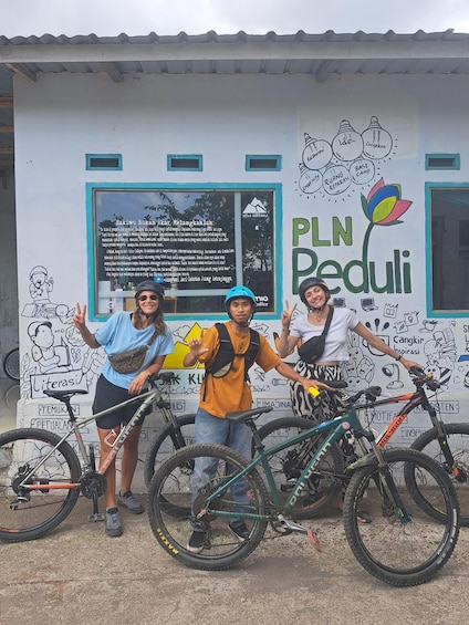 Three people posing with bicycles in front of a wall with educational posters. 2