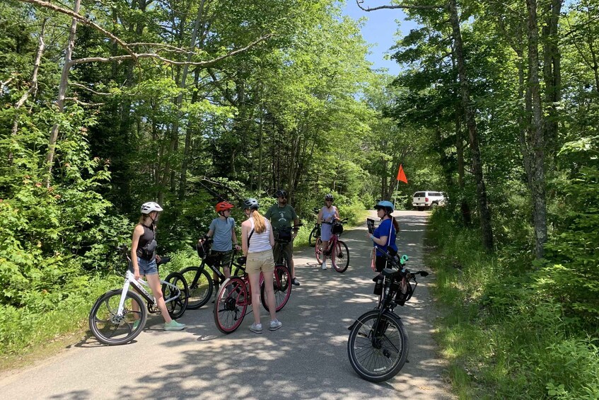 A group of cyclists on a paved path surrounded by trees. 5