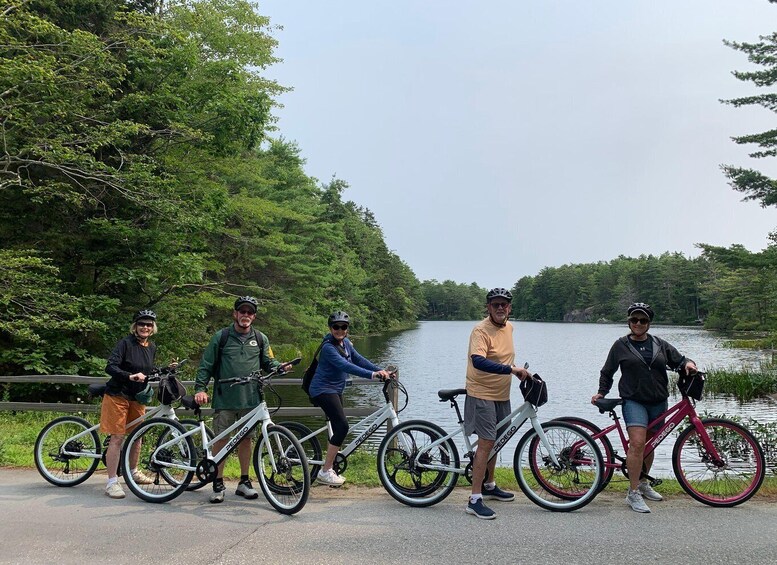 A group of cyclists on a paved path by a lake with trees in the background. 4