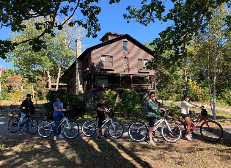 A group of people with bicycles in front of a wooden house surrounded by trees. 3