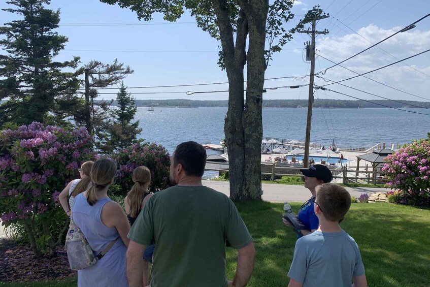 A group of people standing by a waterfront with a dock and a pool area in the background. 2