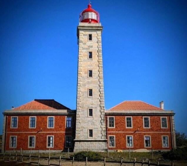 A lighthouse with a red top, a stone tower, and a brick building with a red roof. 3