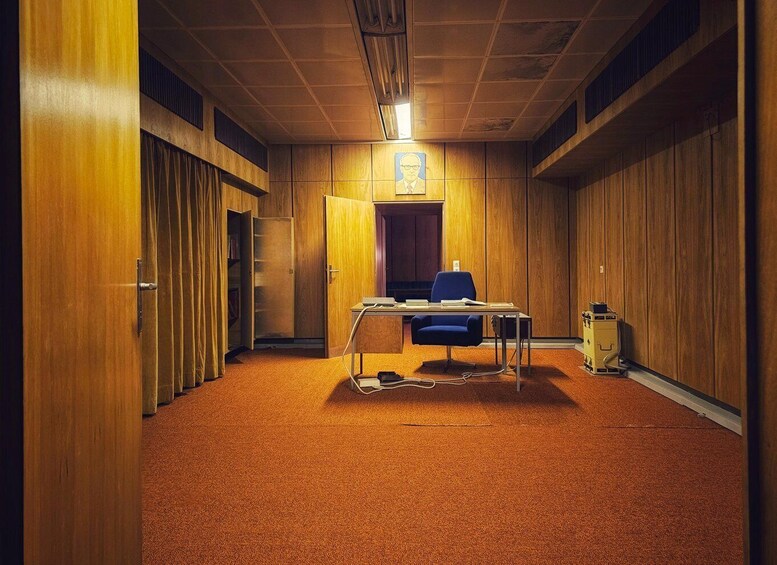 A conference room with wooden walls, a blue chair, a table, and a painting on the wall. 2