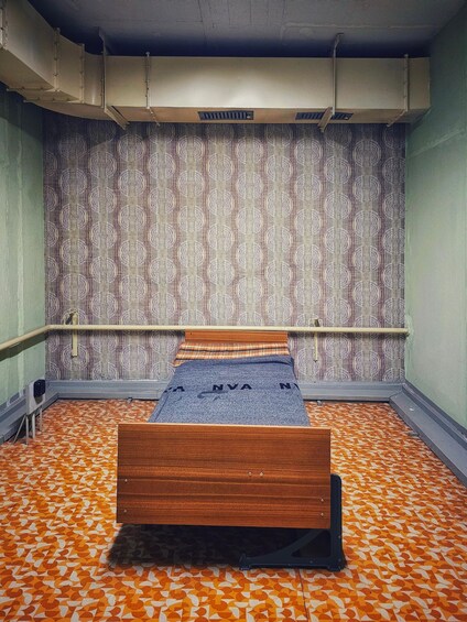 A room with a patterned wallpaper, a wooden bed, and a patterned floor. 3