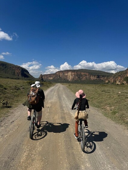Two cyclists on a dirt road with a mountainous landscape in the background. 4
