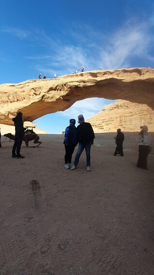 A group of people standing on a desert landscape with a large rock arch formation in the background. 1
