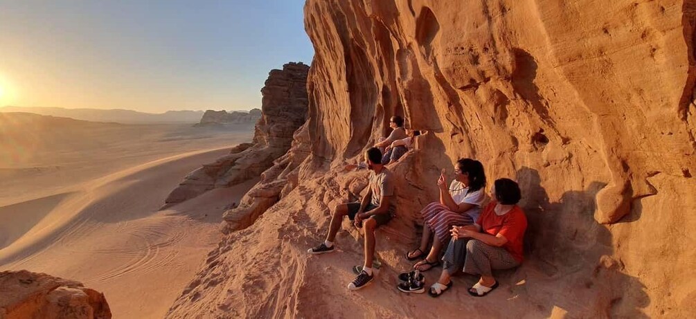 A group of people sitting on a rock formation in a desert landscape. 3