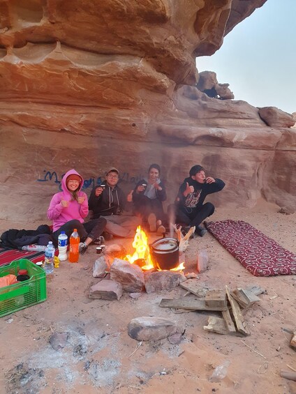 A group of people sitting around a campfire in a rocky outdoor setting. 2
