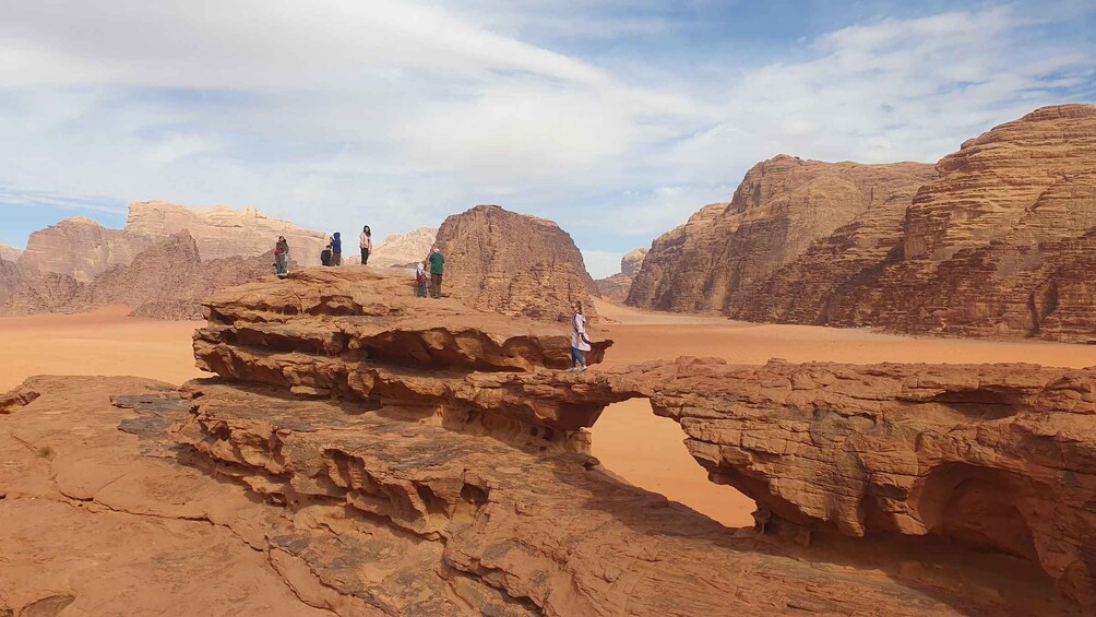 A desert landscape with rock formations and a group of people standing on a rock. 4