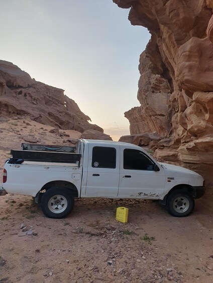 A white pickup truck parked in a rocky canyon with a yellow container nearby. 5