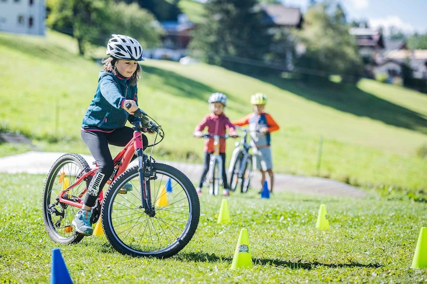 A child riding a bicycle on a grassy path with orange traffic cones. 3