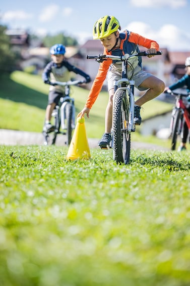 A child on a bicycle navigating a grassy area with a yellow cone. 5