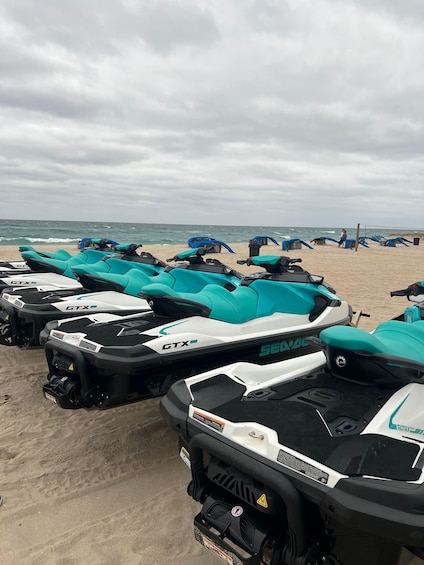 A row of teal and white ATV's on a sandy beach with the ocean in the background. 2