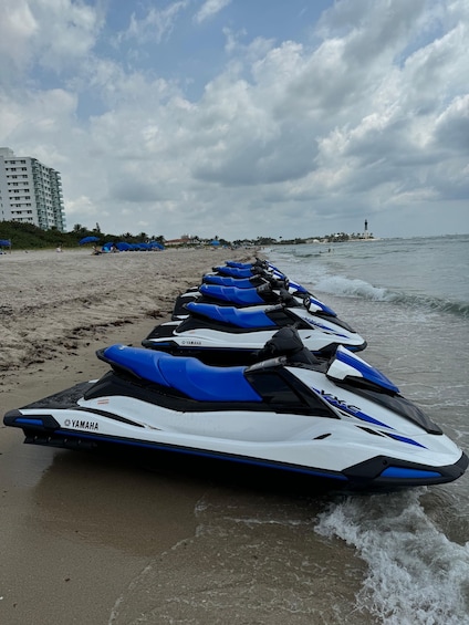 A row of Yamaha jet skis lined up on a beach with a lighthouse in the background. 1
