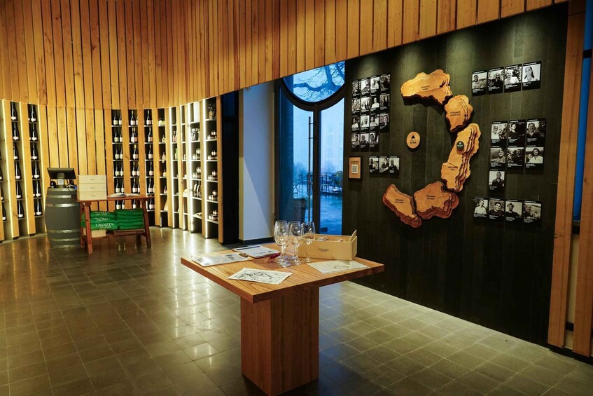 A wine cellar with wooden shelves, a table with wine glasses, and a wall with framed photos. 1