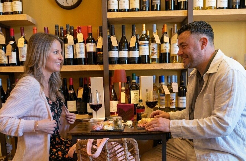 A person and a woman in a wine shop with shelves of wine bottles. 1