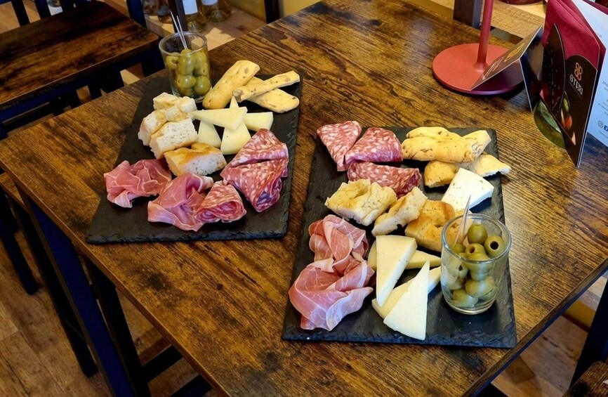A wooden table with two black slate boards holding various cheeses, cured meats, and bread. 5