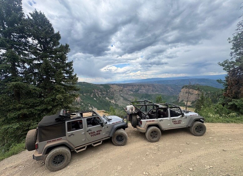 Two off-road vehicles parked on a dirt path with a mountainous landscape in the background. 1