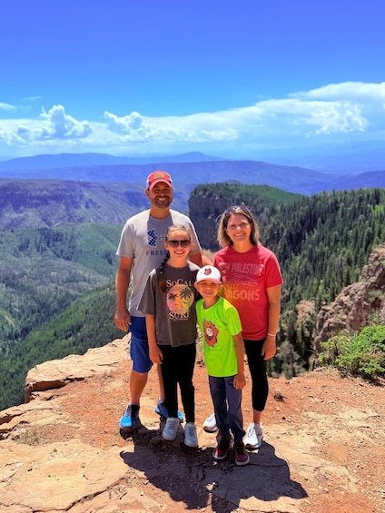 A family of four standing on a rocky outcrop with a mountainous landscape in the background. 3