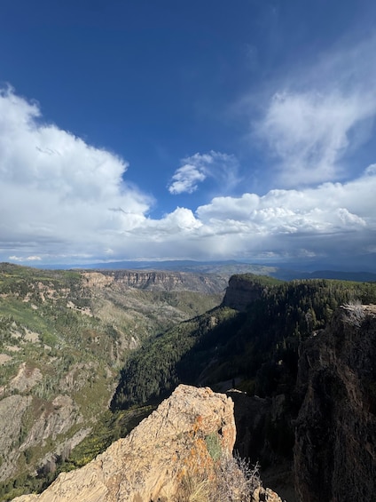 A mountainous landscape with a prominent rocky outcrop in the foreground and a vast valley with dense forests in the background under a partly cloudy sky. 5