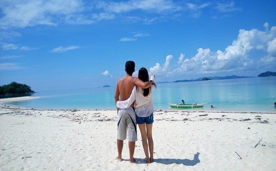 A couple embracing on a beach with a boat in the water and a distant island. 2
