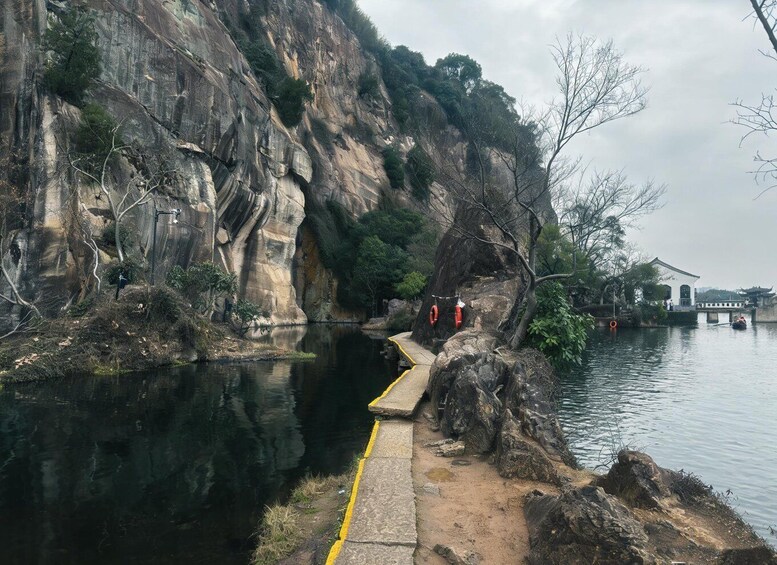 A rocky riverbank with a narrow concrete path, a bridge, and a traditional building across the water. 2