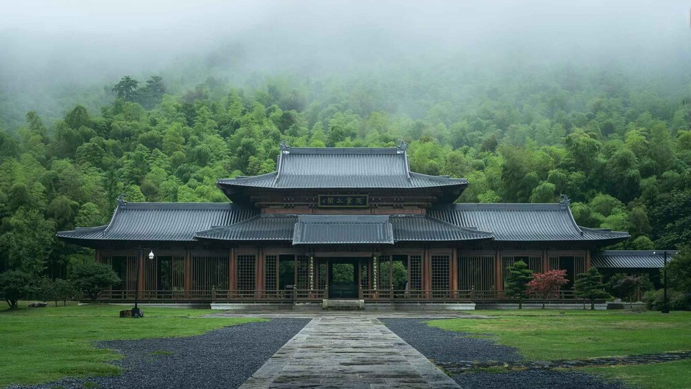 A traditional Japanese building with a tiled roof, surrounded by lush greenery and a misty forest backdrop. 1