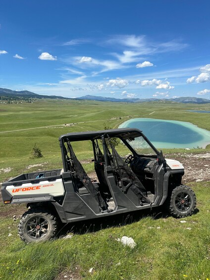 A UForce 1000XL off-road vehicle parked on grass near a turquoise lake with mountains in the background. 3